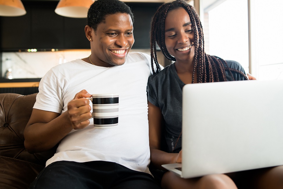 Couple using laptop while sitting on couch at home.